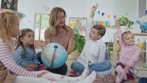 A pre- school teacher sitting on floor and teaching geography children indoors in nursery, montessori education.