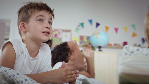 Preschool children in a pajamas lying in beds ready for nap indoors in nursery school.