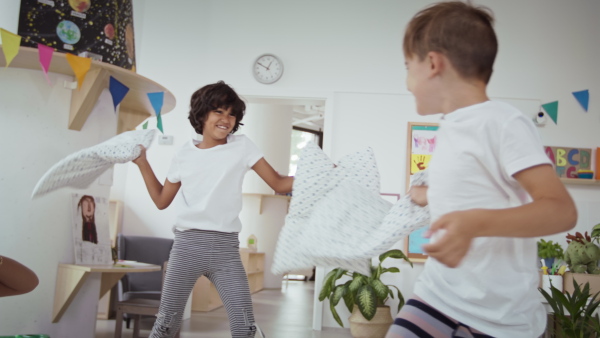 Preschool children in pajamas having fun, pillow fighting indoors in a nursery school.