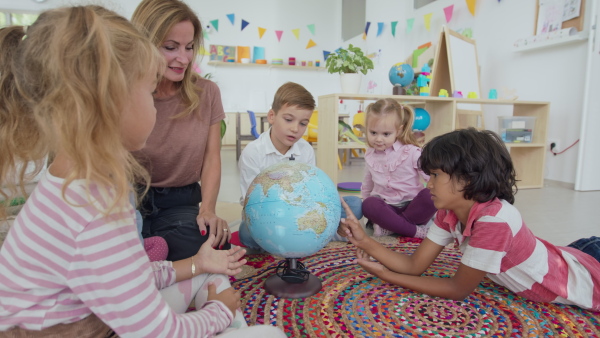 A pre- school teacher sitting on floor and teaching geography children indoors in nursery, montessori education.