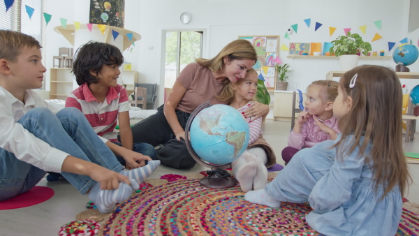 A pre- school teacher sitting on floor and teaching geography children indoors in nursery, montessori education.