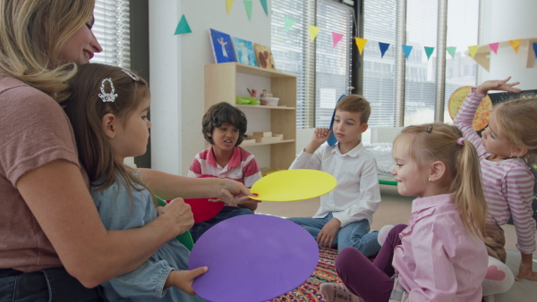 A multicultural group of small children with teacher sitting on carpet and playing at kindergarten.