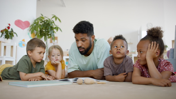 A group of small nursery school children with man teacher on floor indoors in classroom, reading book.