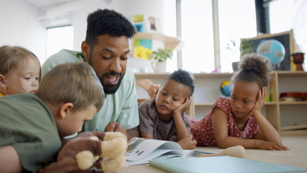 A group of small nursery school children with man teacher on floor indoors in classroom, reading book.