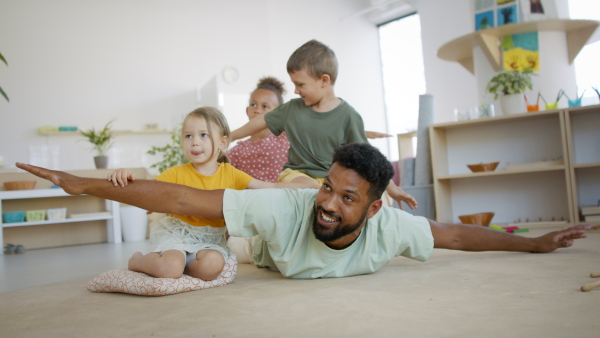 A group of small nursery school children with man teacher sitting on floor indoors in classroom, playing.