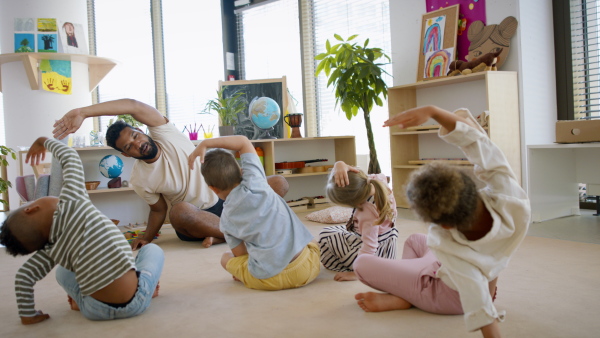 A group of small nursery school children with teacher on floor indoors in classroom, exercising.