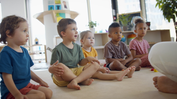 A group of small nursery school children with man teacher sitting on floor indoors in classroom, having lesson.