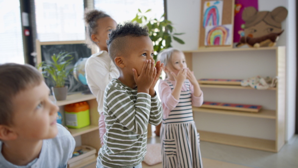 A group of small nursery school children indoors in classroom, doing exercise.