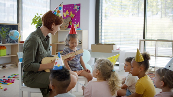 A group of small nursery school children with teacher on floor indoors in classroom, celebration concept.