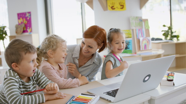 A group of small nursery school children with teacher indoors in classroom, using laptop.