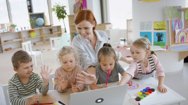 A group of small nursery school children with teacher indoors in classroom, using laptop.