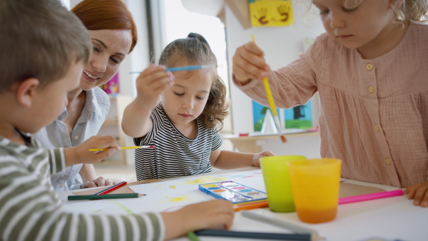 A group of small nursery school children with teacher indoors in classroom, painting.