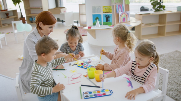 A group of small nursery school children with teacher indoors in classroom, painting.