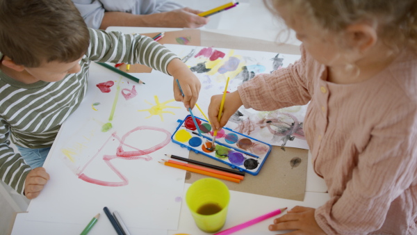 A top view of group of small nursery school children with teacher indoors in classroom, painting.