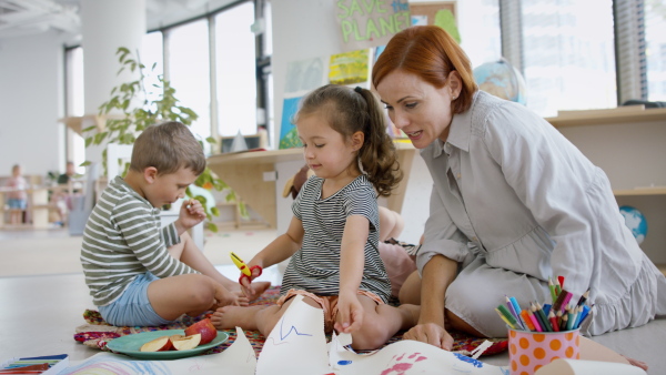 A group of small nursery school children with teacher indoors in classroom, art and craft concept.