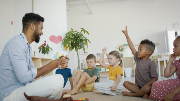 A group of small nursery school children with man teacher sitting on floor indoors in classroom, having lesson.