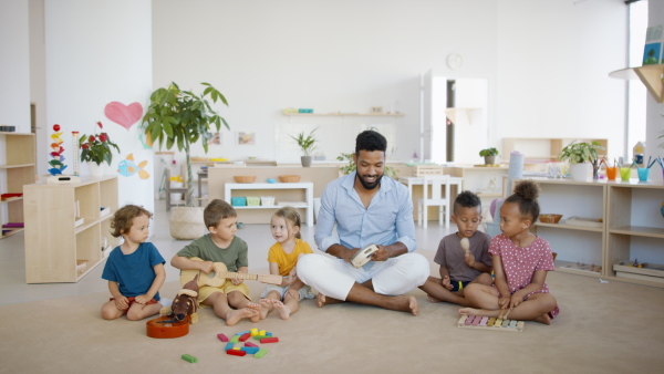 A group of small nursery school children with man teacher sitting on floor indoors in classroom, having music lesson.