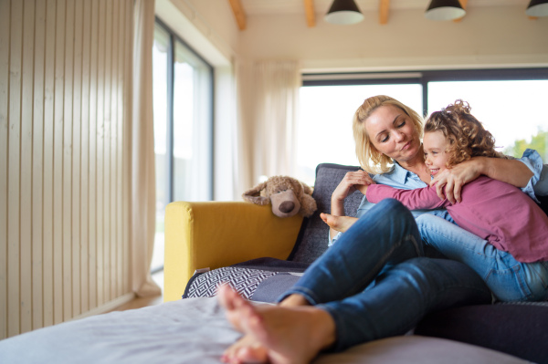 A cute small girl with mother on sofa indoors at home, resting. Copy space.