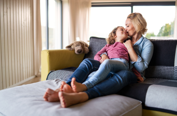 A cute small girl with mother on sofa indoors at home, kissing when resting.