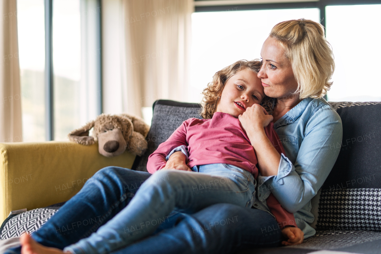 A cute small girl with mother on sofa indoors at home, resting.