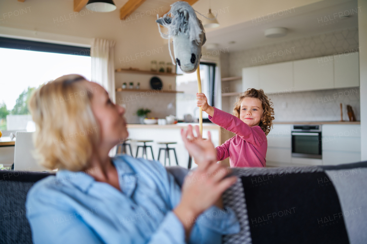 A happy cute small girl with mother indoors at home, playing.