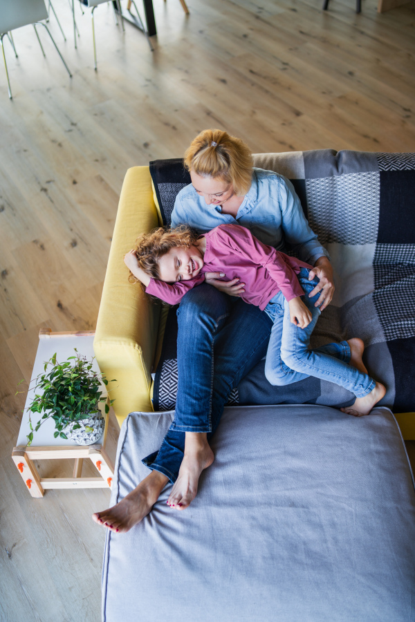 A top view of cute small girl with mother on sofa indoors at home, resting.