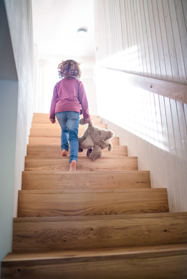 A rear view of small girl walking up wooden stairs indoors at home. Copy space.