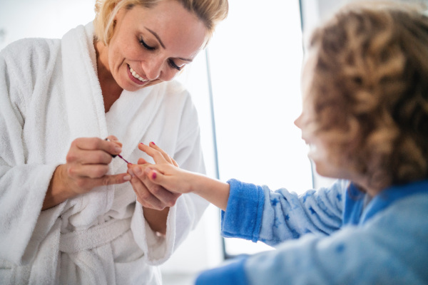 A happy cute small girl with mother in bathroom indoors at home, painting nails.