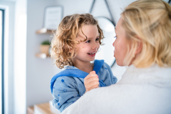 A cute small girl with unrecognizable mother in bathroom indoors at home, talking.