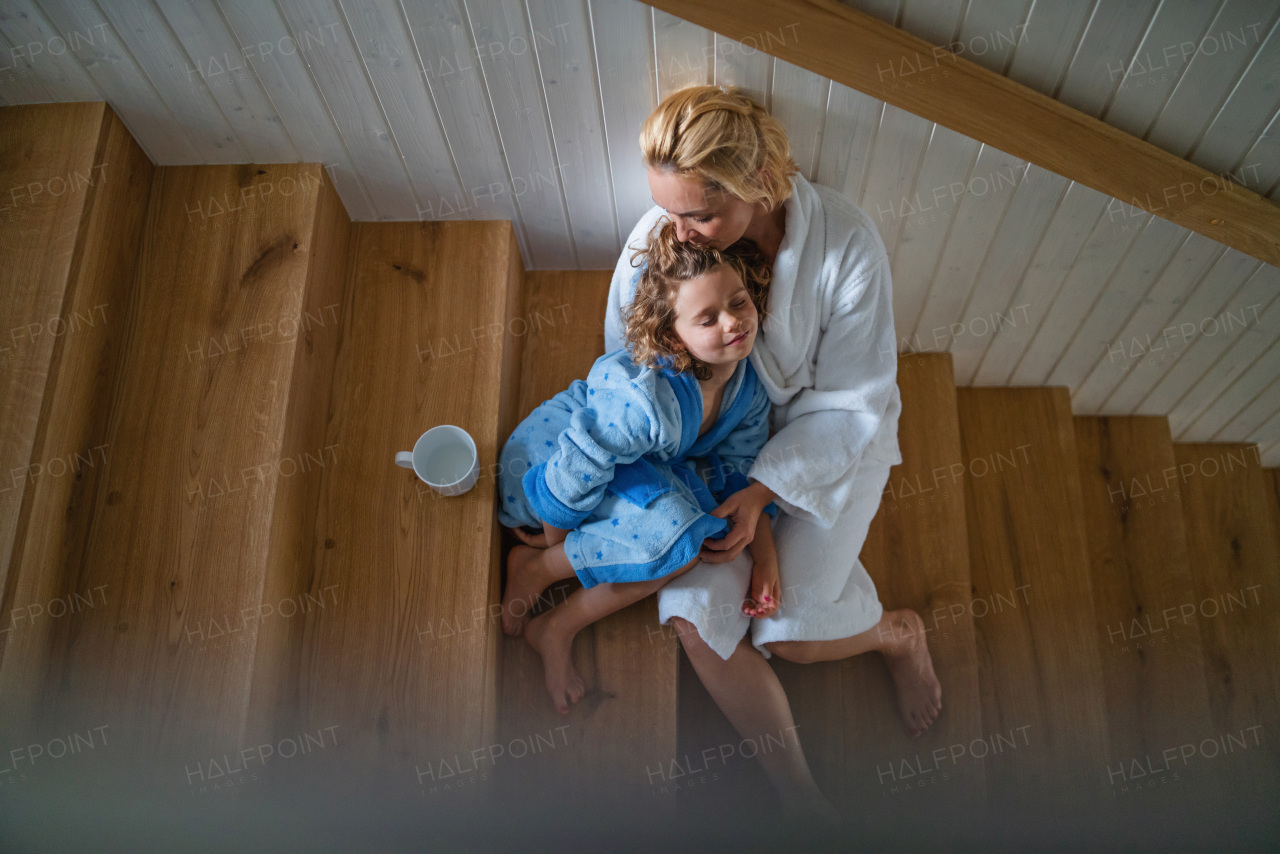 A top view of small girl with mother indoors at home, sitting on stairs in the morning.