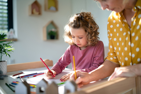 A cute small girl with mother in bedroom indoors at home, drawing pictures.