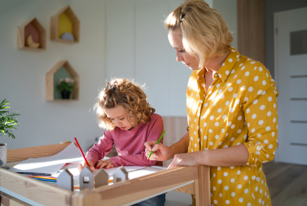 A cute small girl with mother in bedroom indoors at home, drawing pictures.