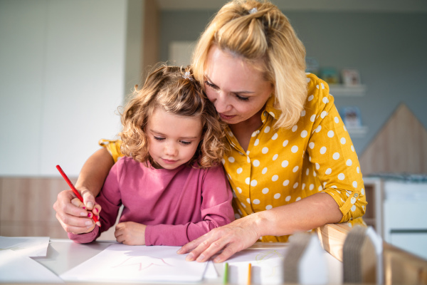 A cute small girl with mother in bedroom indoors at home, drawing pictures.