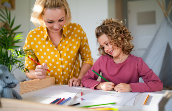 A cute small girl with mother in bedroom indoors at home, drawing pictures.