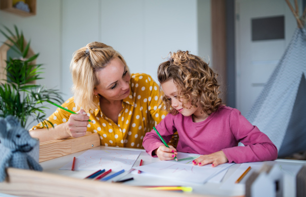 A cute small girl with mother in bedroom indoors at home, drawing pictures.