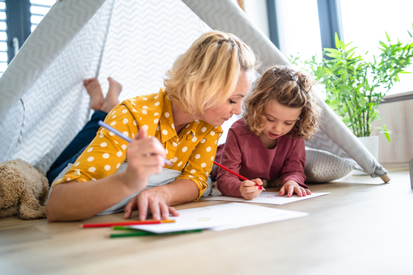 A cute small girl with mother in bedroom indoors at home, drawing pictures.