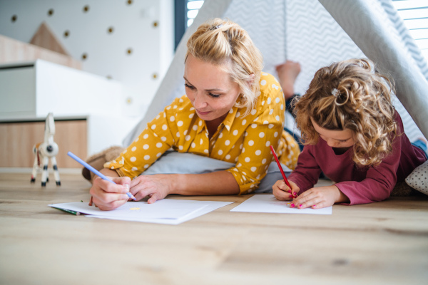 A cute small girl with mother in bedroom indoors at home, drawing pictures.