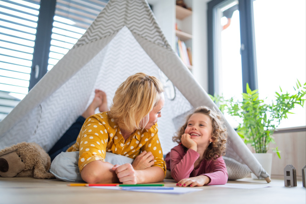 A front view of cute small girl with mother indoors at home, playing.