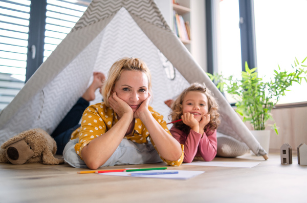 A front view of cute small girl with mother indoors at home, playing.