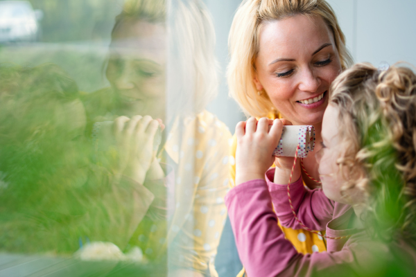 A cute small girl with mother indoors at home, playing with toy binoculars. Copy space.