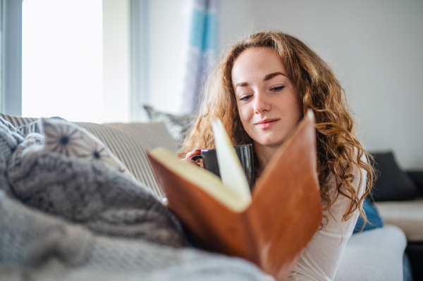 Young woman relaxing indoors at home with coffee and book.