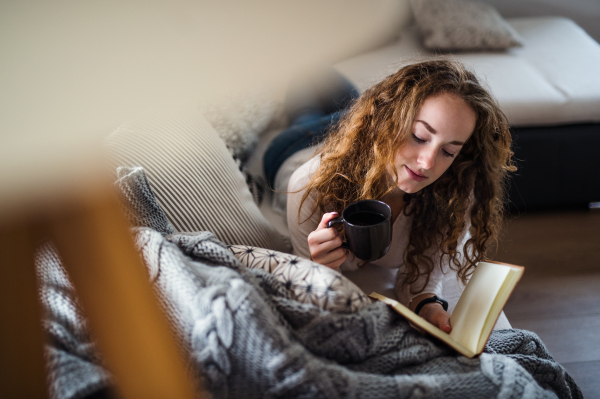 Young woman relaxing indoors at home with coffee and book.