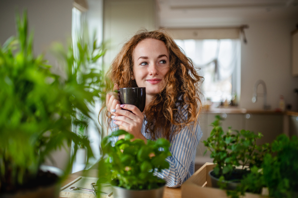 Front view of young woman relaxing indoors at home with cup of coffee or tea.