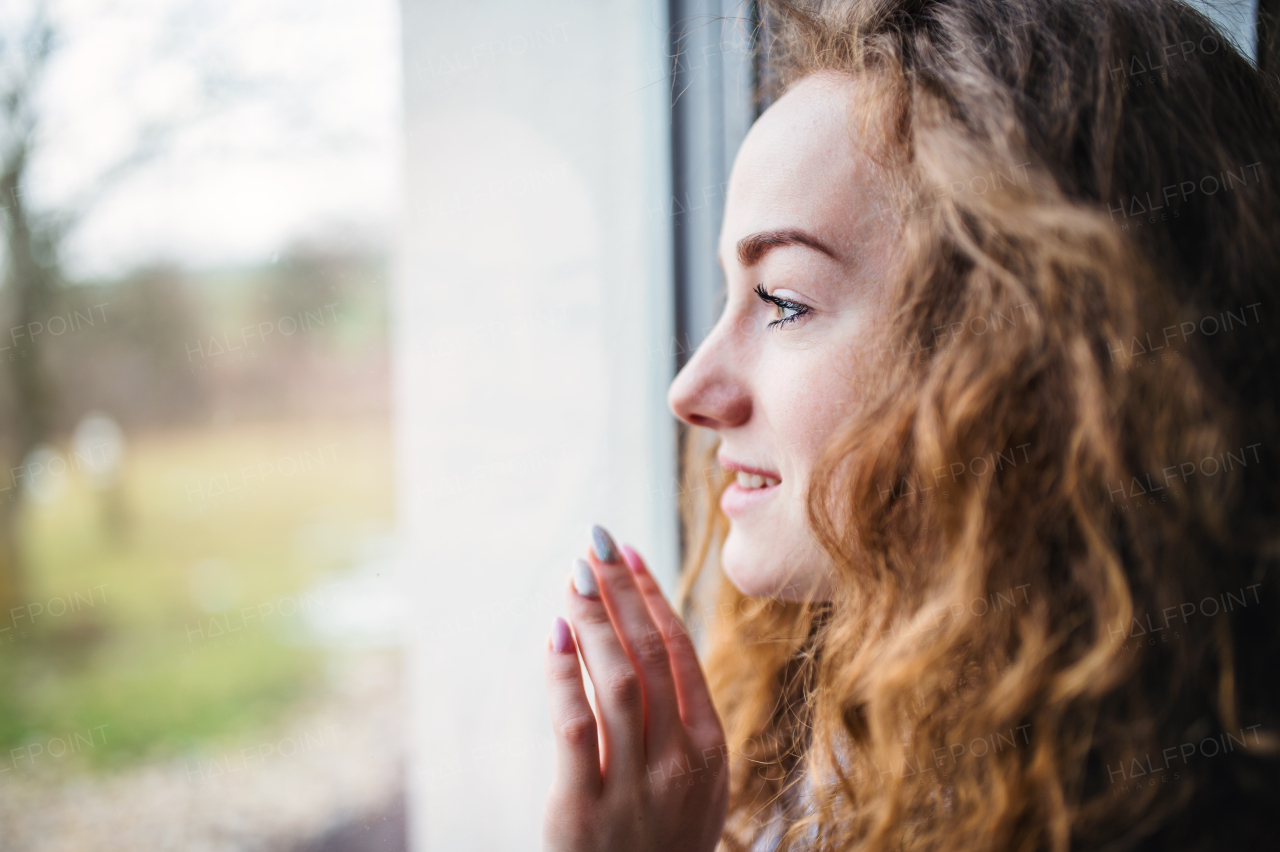 Close-up portrait of young woman standing by window indoors at home. Copy space.