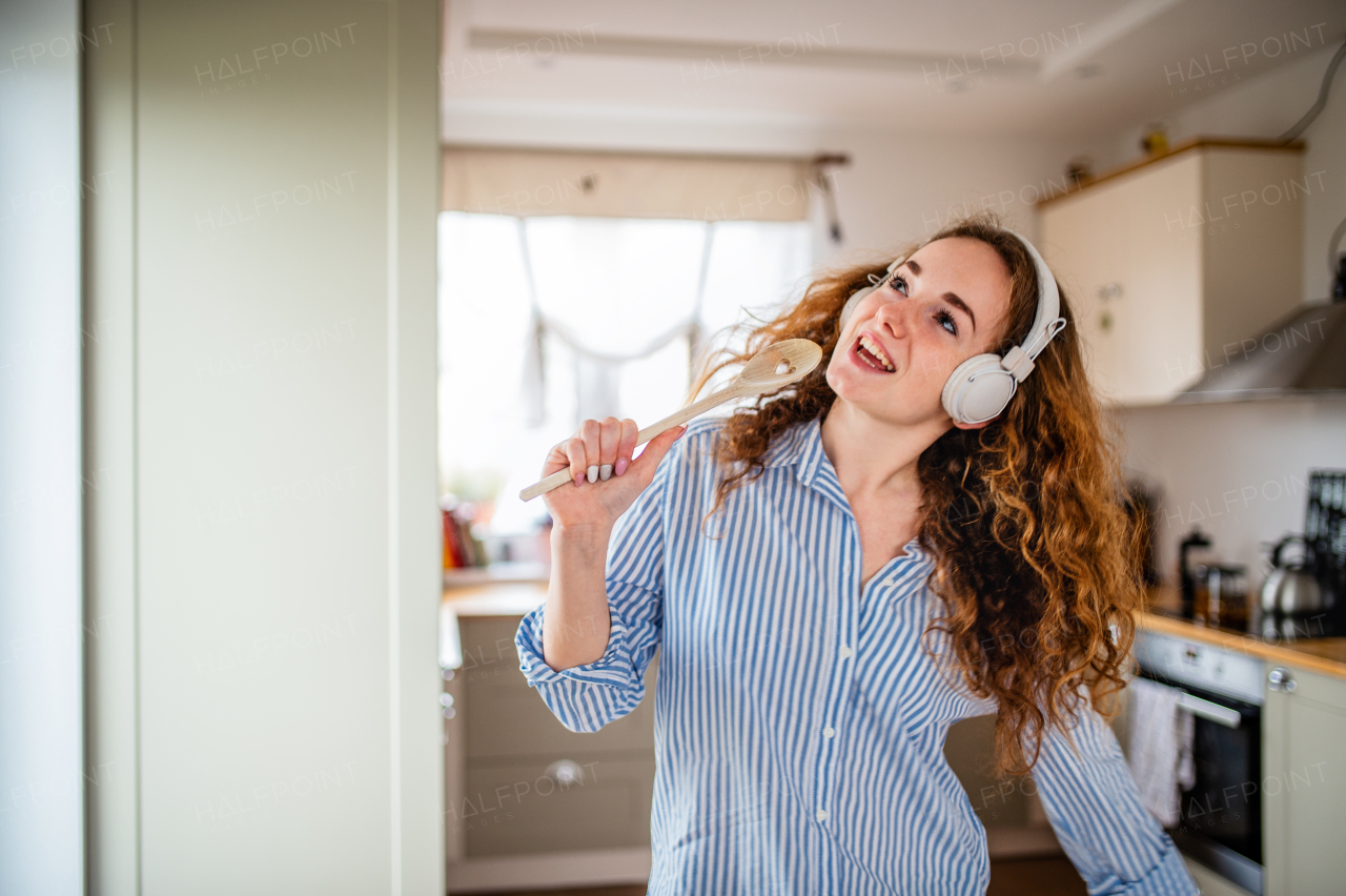 Young woman with headphones relaxing indoors at home, listening to music and singing.