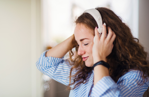 Young woman with headphones relaxing indoors at home, listening to music.