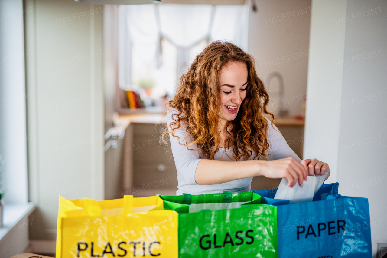 Front view of young woman indoors at home separating glass, paper, and plastic waste.