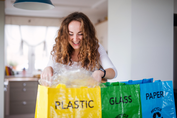 Front view of young woman indoors at home separating glass, paper, and plastic waste.