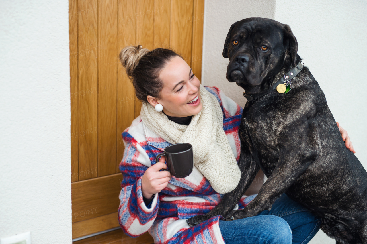 Young woman relaxing outdoors by front door at home with coffee and pet dog.