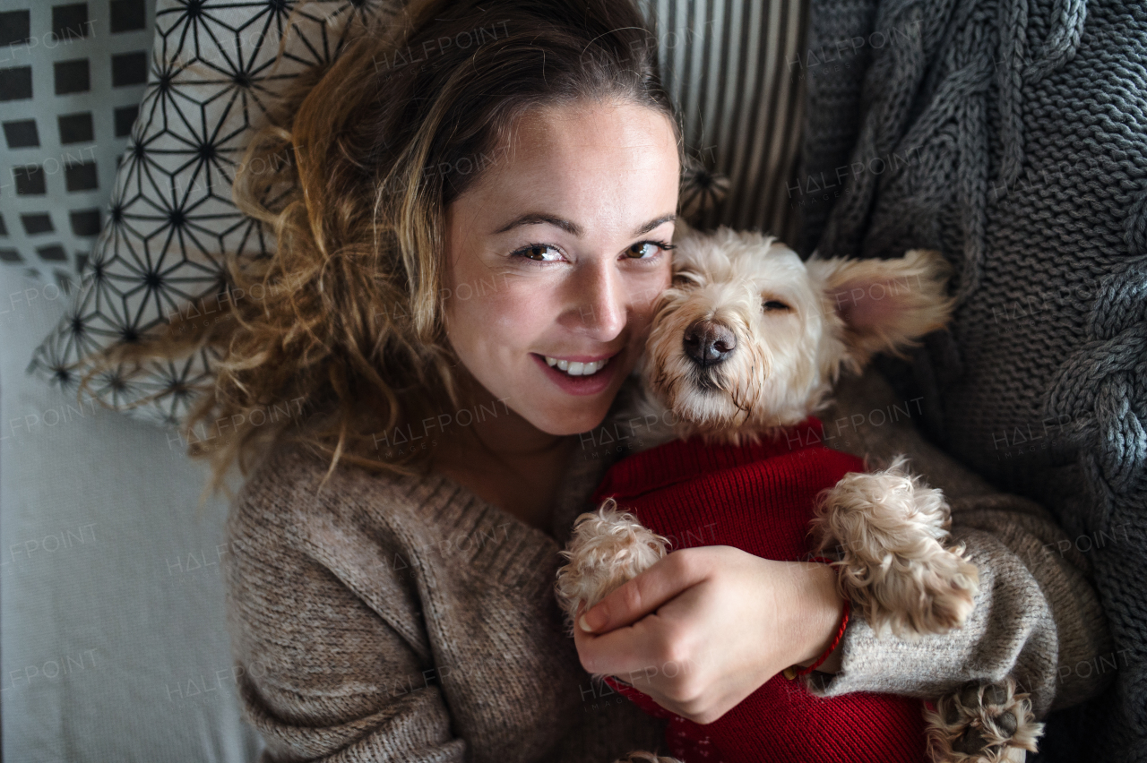 Top view of young woman relaxing indoors on sofa at home with pet dog.